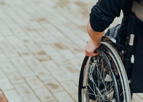 Close-up of male hand on wheel of wheelchair during walk in park. He holds his hands on the wheel.